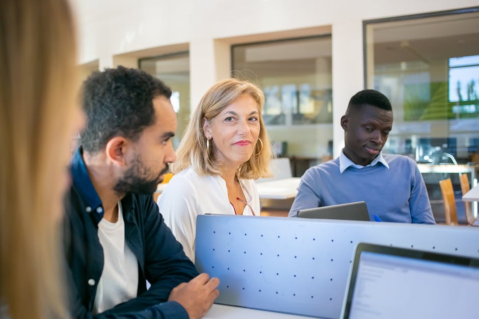 A diverse group of students working together in a university classroom setting with laptops and casual attire.