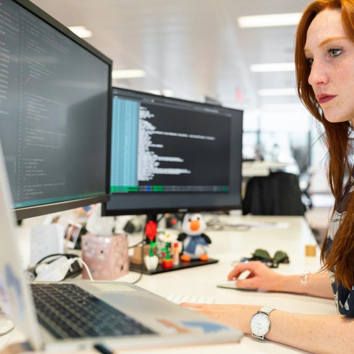 A focused female software engineer coding on dual monitors in a modern office.